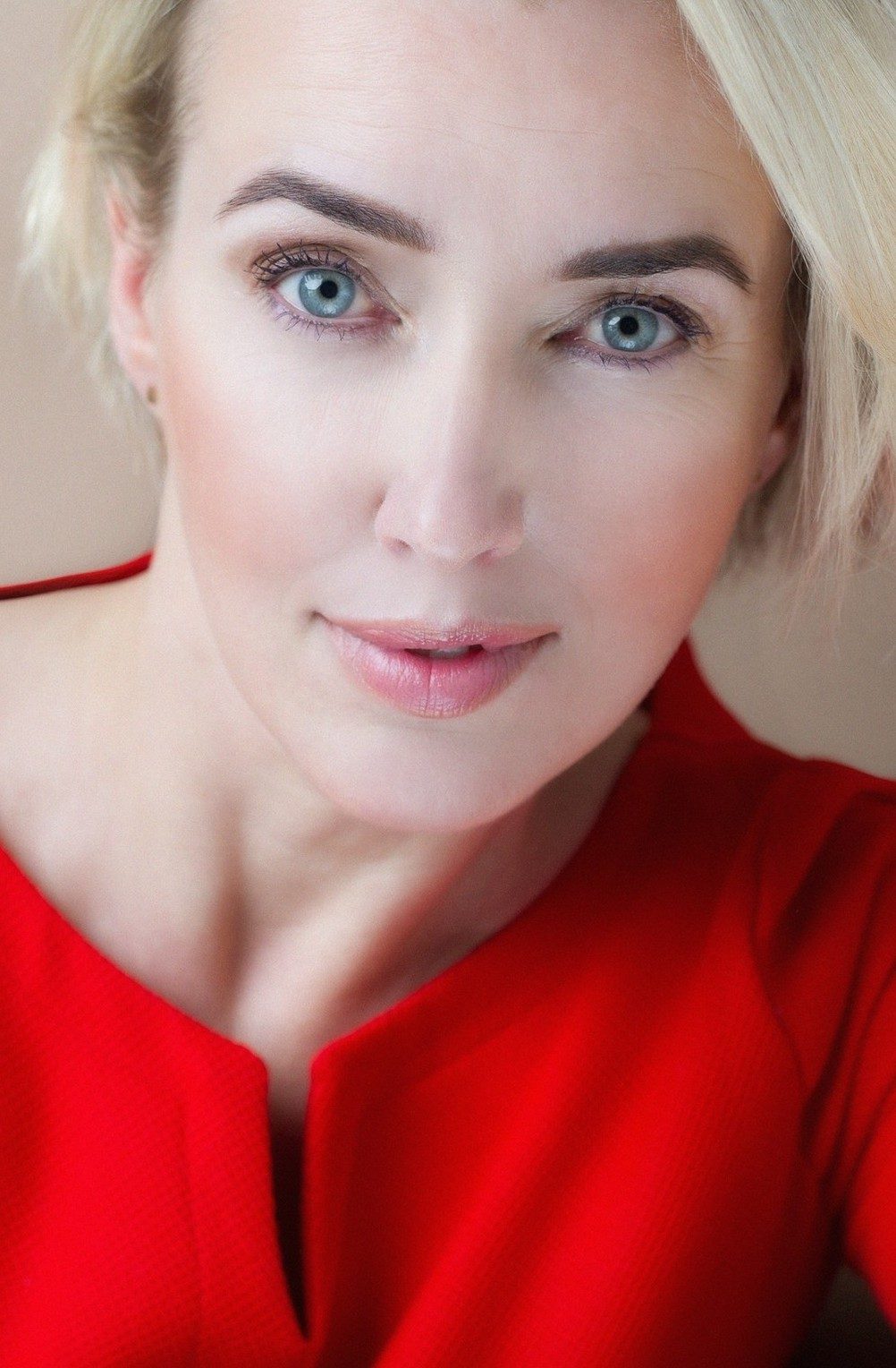 Nahes Beautyportrait einer blonden Frau mit blauen Augen in roter Bluse vor beigem Hintergrund — Das Studiozwei, Werbefotograf München