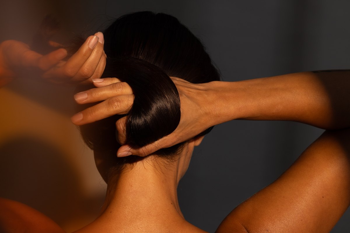 Haende formen einen Haarknoten im Nacken, warmes Streiflicht auf der Haut — Das Studiozwei, Werbefotograf München