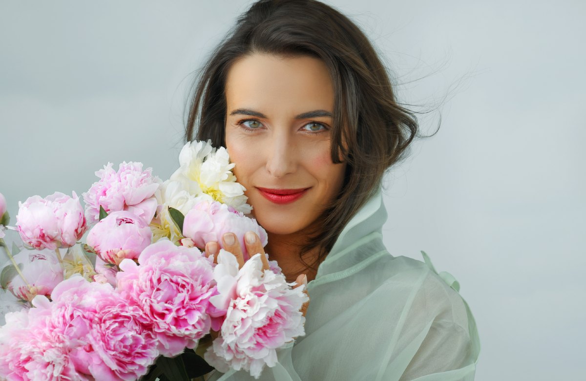 Frau in mintfarbener Bluse haelt einen Strauss rosa Pfingstrosen — Das Studiozwei, Werbefotograf München