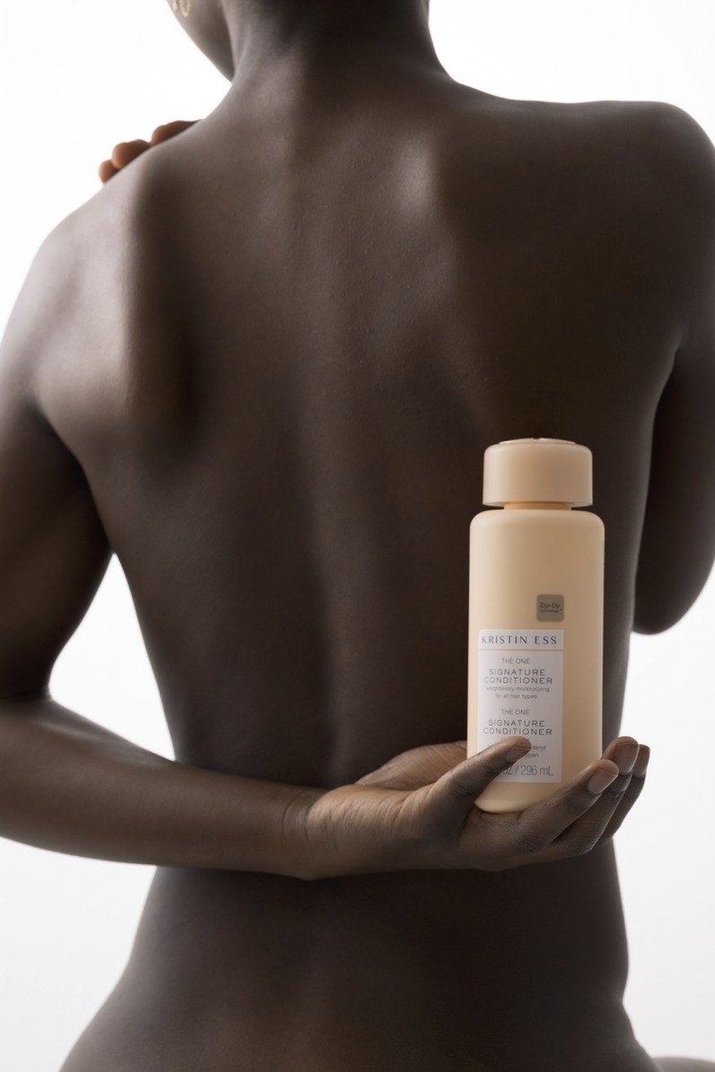 Ruecken einer Frau, die vor dem Koerper eine cremefarbene Kristin Ess Conditioner Flasche haelt — Das Studiozwei, Werbefotograf München