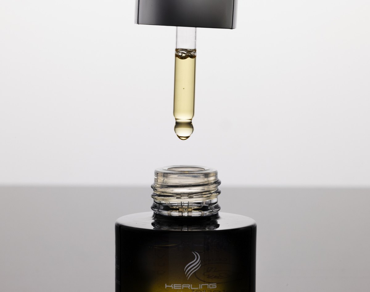 Goldgelber Oeltropfen haengt an einer Pipette ueber der geoeffneten Kerling Hair Oil Flasche — Das Studiozwei, Werbefotograf München