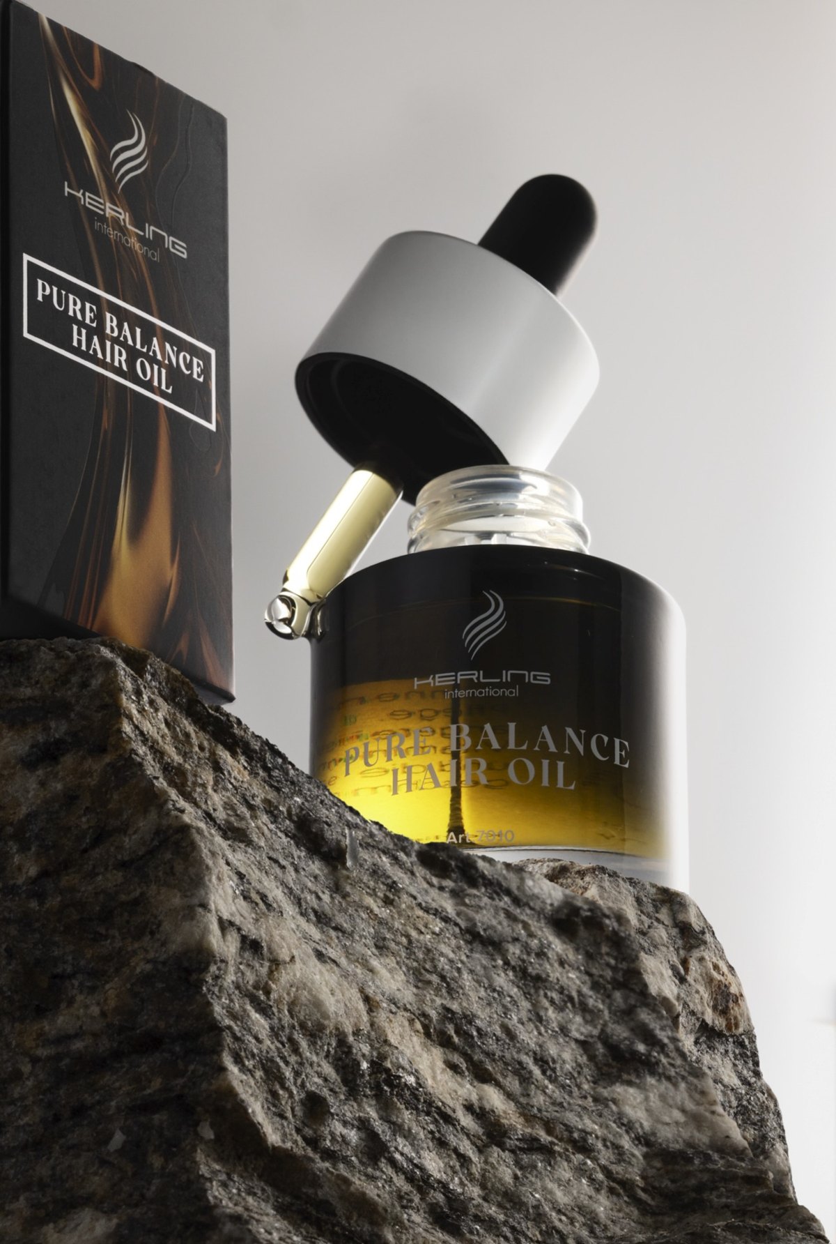 Kerling Pure Balance Hair Oil Flasche mit goldenem Oel auf rohem Steinblock neben der Verpackung — Das Studiozwei, Werbefotograf München