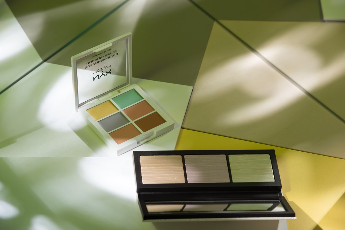 NYX Color Concealer Palette und eine Highlighter-Palette auf gruen gefiltertem Untergrund im Blattschatten — Das Studiozwei, Werbefotograf München