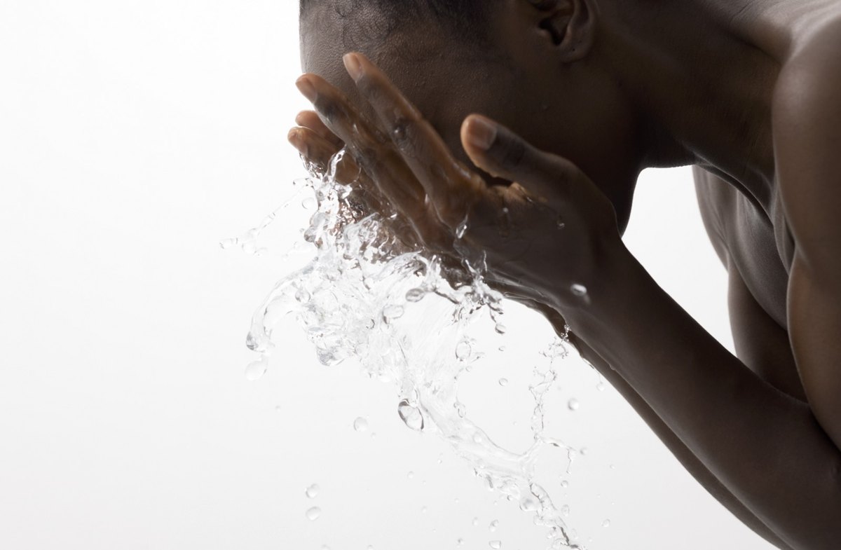 Mann mit dunkler Haut beugt sich vor und spritzt sich mit beiden Haenden Wasser ins Gesicht — Das Studiozwei, Werbefotograf München