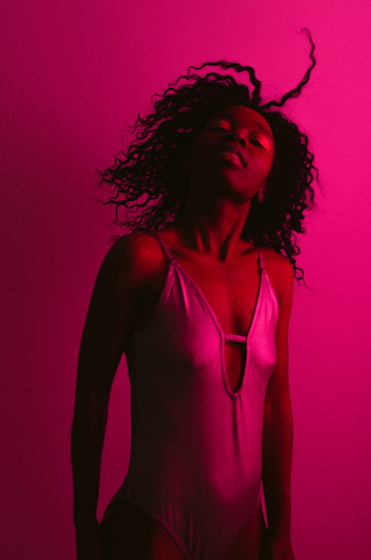 Model im hellen Bodysuit mit fliegenden Locken vor magentafarbenem Hintergrund in farbigem Gel-Licht — Das Studiozwei, Werbefotograf München
