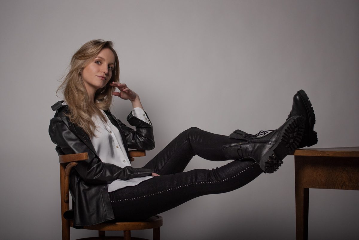 Blonde Frau in Lederjacke und Boots sitzt auf einem Stuhl mit Beinen auf dem Tisch — Das Studiozwei, Werbefotograf München