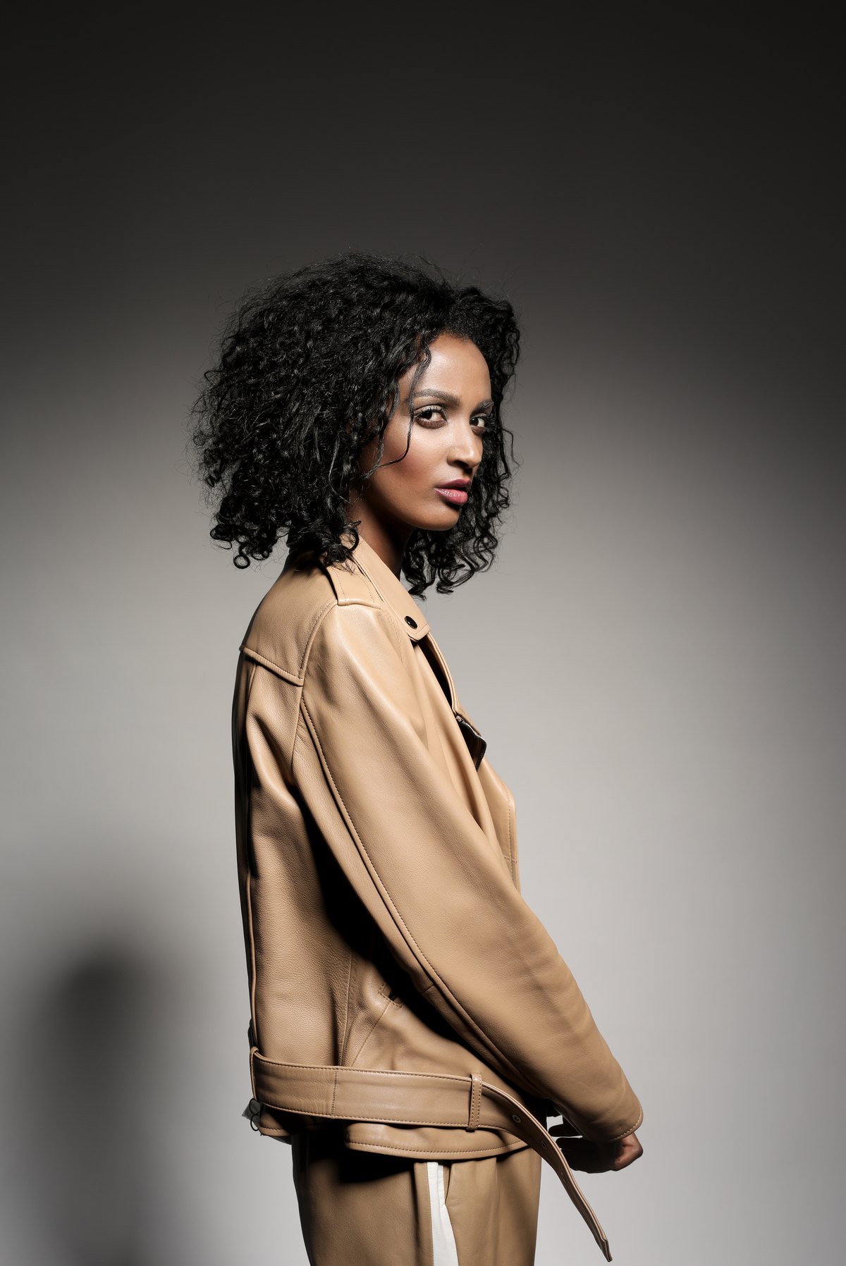 Model in camelfarbener Lederjacke im Halbprofil vor grauem Verlauf — Das Studiozwei, Werbefotograf München