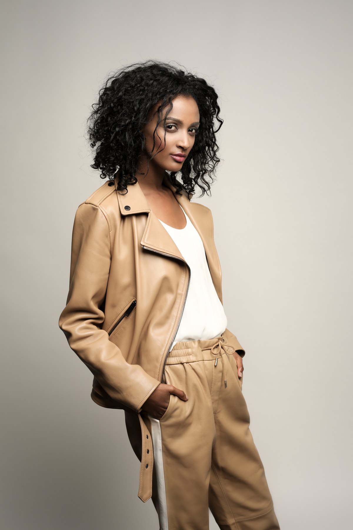 Model in camelfarbener Lederjacke und heller Hose vor grauem Studiohintergrund — Das Studiozwei, Werbefotograf München