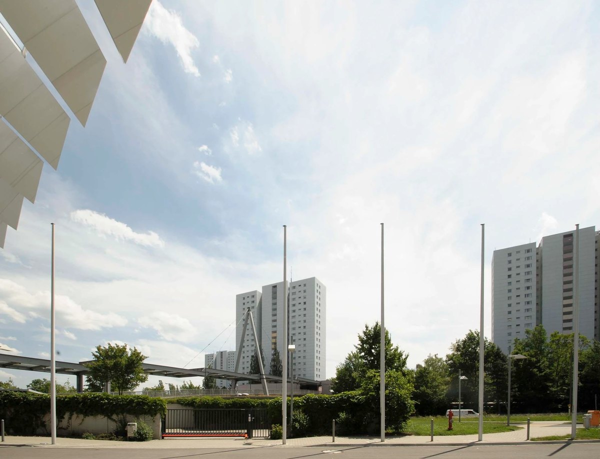 Fahnenmasten vor Wohnhochhaeusern und weissem Dachtragwerk unter weitem Wolkenhimmel — Das Studiozwei, Werbefotograf München
