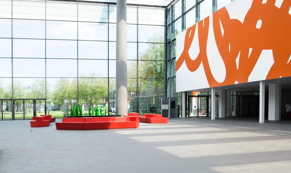 Helles Foyer mit roten Sitzinseln, Glasfassade und grossem orangefarbenem Wandbild — Das Studiozwei, Werbefotograf München