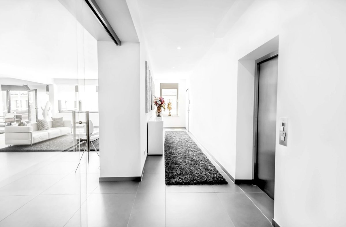 Heller Flur mit Glaswand, dunklem Laeufer und Aufzugstuer aus Edelstahl — Das Studiozwei, Werbefotograf München