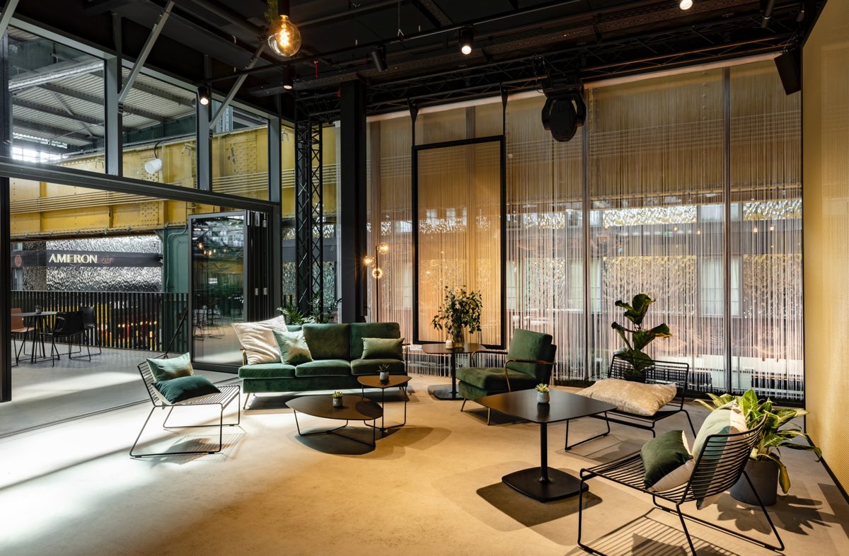 Weiter Blick in einen Lounge-Bereich mit gruenen Samtsofas, Glaswand und offener Deckenkonstruktion — Das Studiozwei, Werbefotograf München