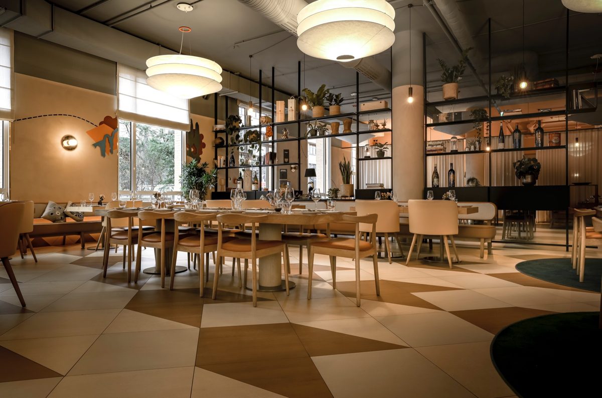 Heller Gastraum mit langer eingedeckter Tafel, Musterboden und grossen Schirmleuchten — Das Studiozwei, Werbefotograf München