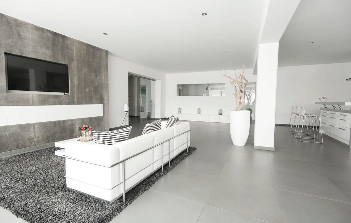 Wohnzimmer mit weisser Sofagarnitur, Betonoptikwand und offener Kuecheninsel — Das Studiozwei, Werbefotograf München