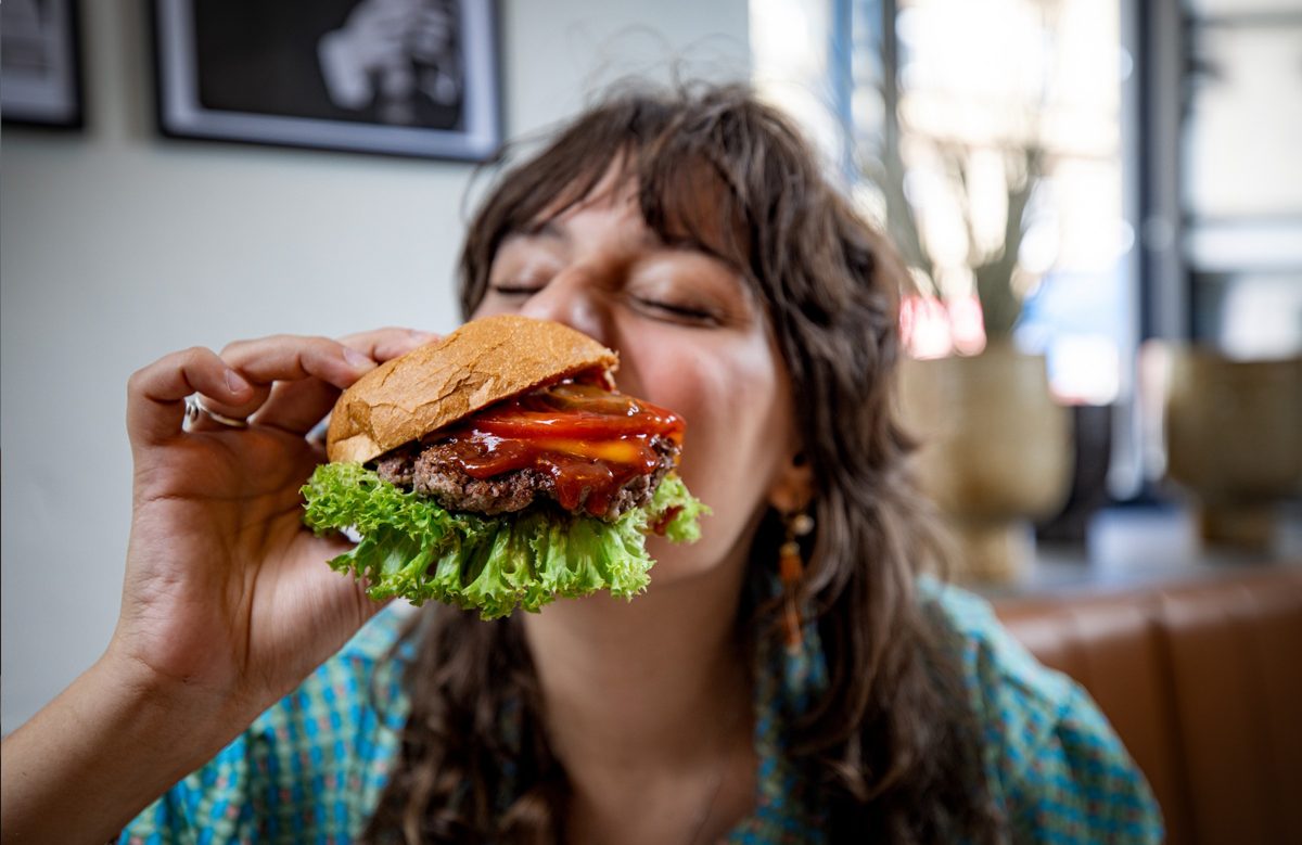 Frau beisst genussvoll in einen Burger in einem Restaurant — Das Studiozwei, Werbefotograf München
