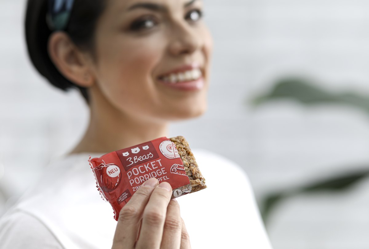 Laechelnde Frau haelt einen verpackten Snackriegel in die Kamera — Das Studiozwei, Werbefotograf München