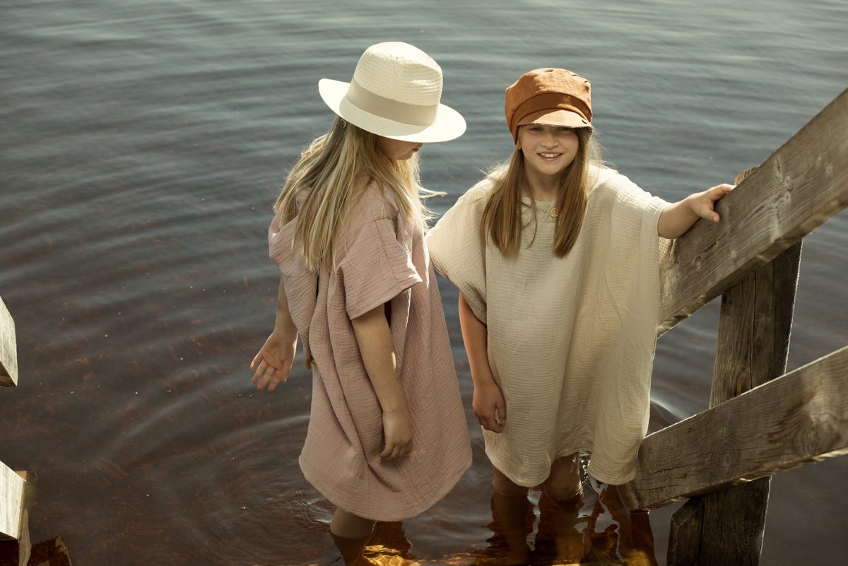 Zwei Kinder in Musselin-Ponchos stehen im flachen Wasser eines Sees im warmen Abendlicht — Das Studiozwei, Werbefotograf München