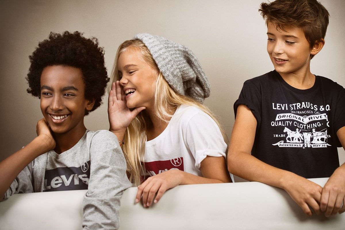 Drei lachende Kinder an einer weissen Bruestung vor warm beigem Hintergrund — Das Studiozwei, Werbefotograf München