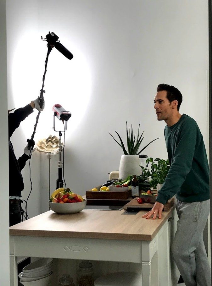 Mann an einer Kuecheninsel mit Obst und Kraeutern waehrend einer Aufnahme mit Mikrofonangel und Licht — Das Studiozwei, Werbefotograf München