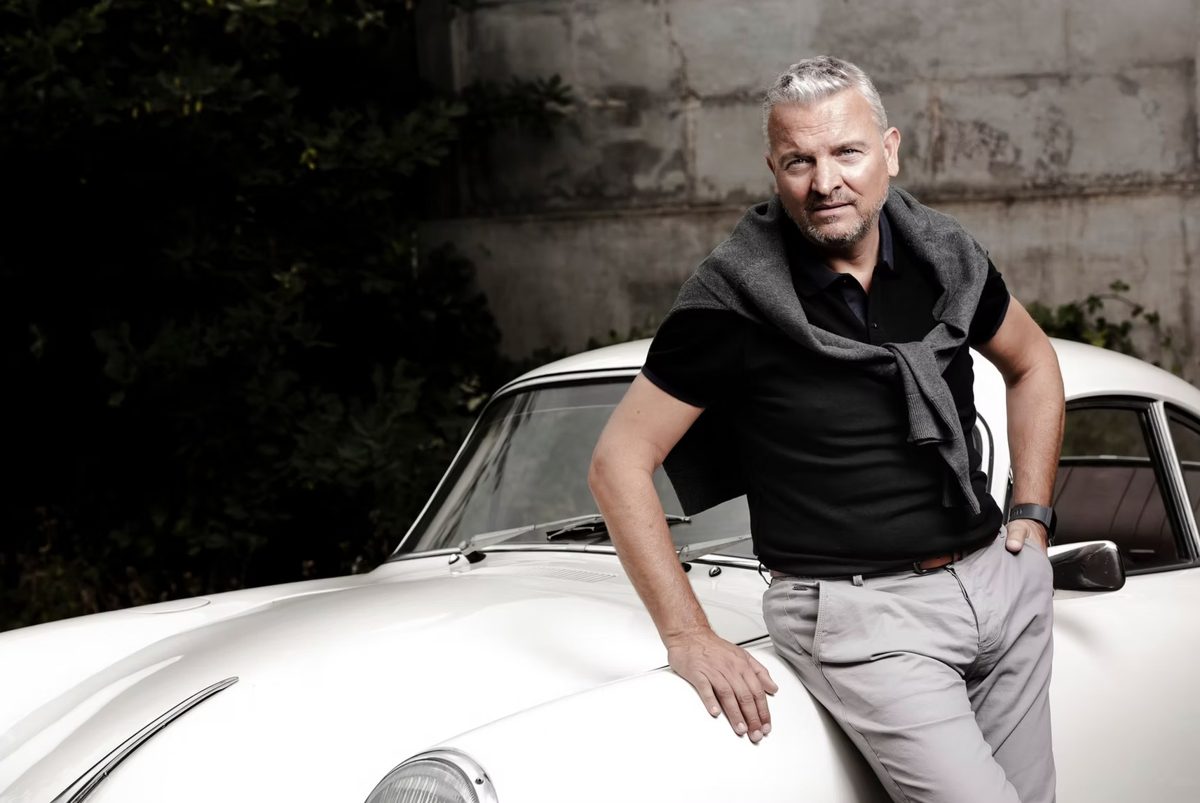 Mann in schwarzem Polo lehnt an einem weissen Oldtimer-Sportwagen vor Betonwand — Das Studiozwei, Werbefotograf München