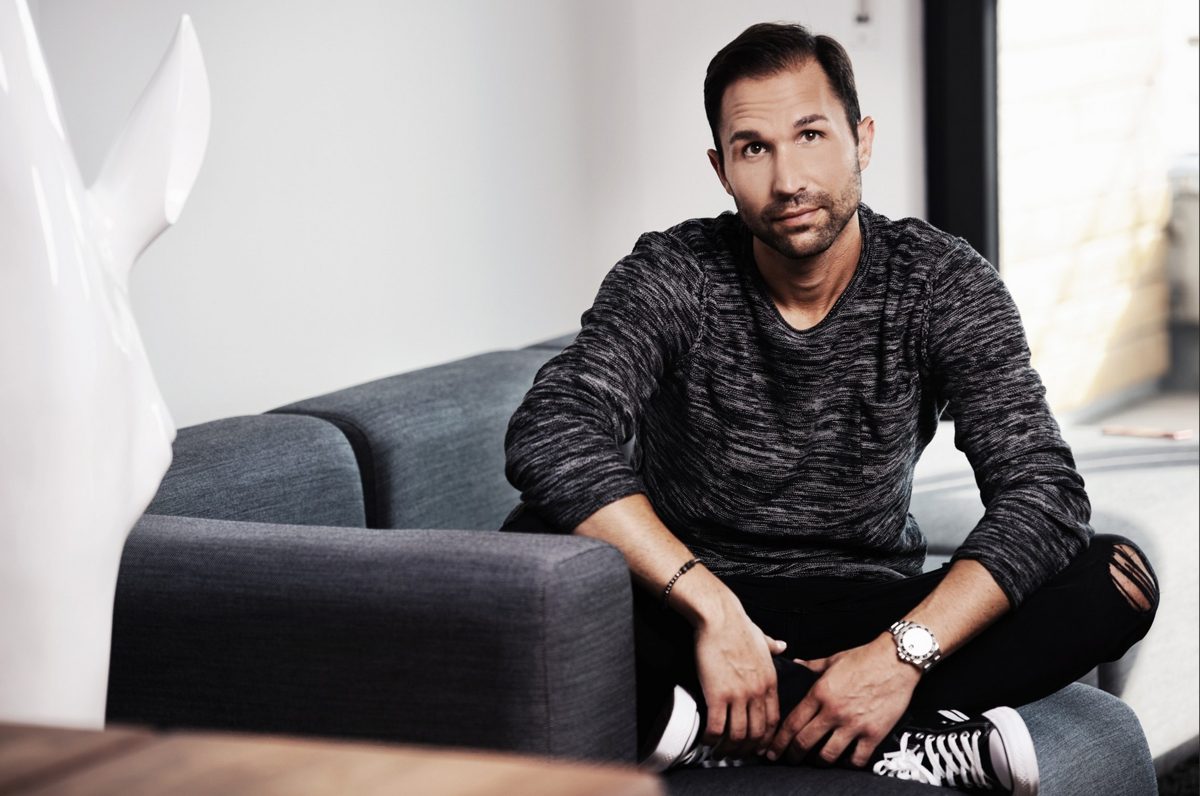 Mann im melierten Pullover sitzt auf einem grauen Sofa in hellem Wohnraum — Das Studiozwei, Werbefotograf München