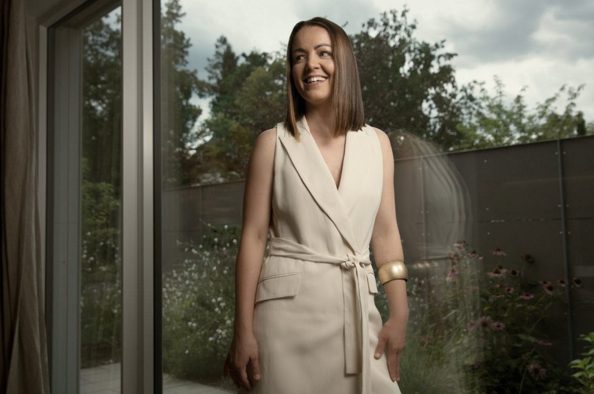 Businessportrait einer laechelnden Frau im cremefarbenen Kleid an einer Glastuer mit Gartenblick — Das Studiozwei, Werbefotograf München