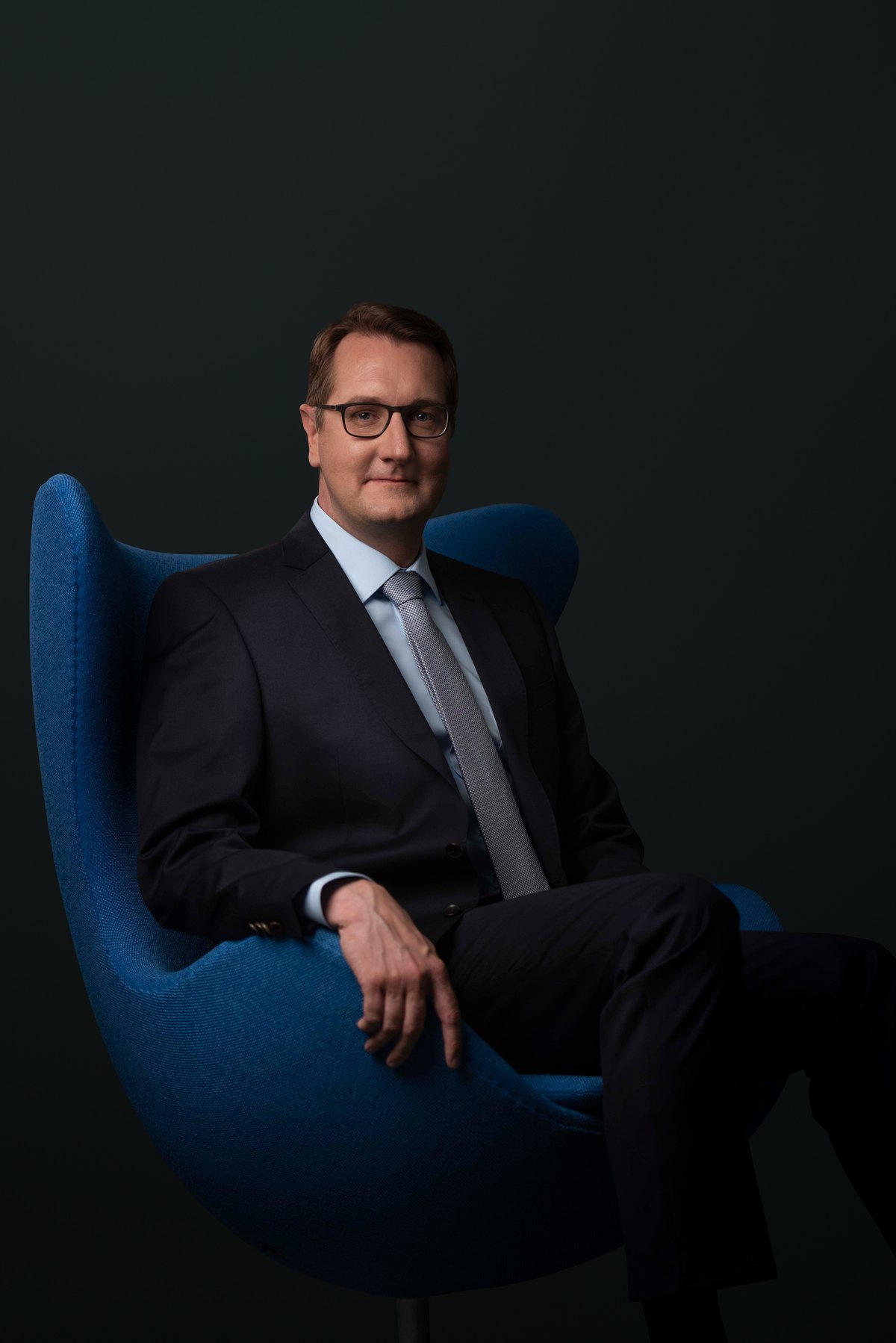 Mann im Anzug sitzt in einem blauen Designsessel — Das Studiozwei, Werbefotograf München