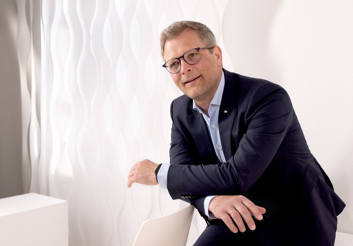 Mann mit Brille im Anzug sitzt vor gewellter weisser Wand — Das Studiozwei, Werbefotograf München