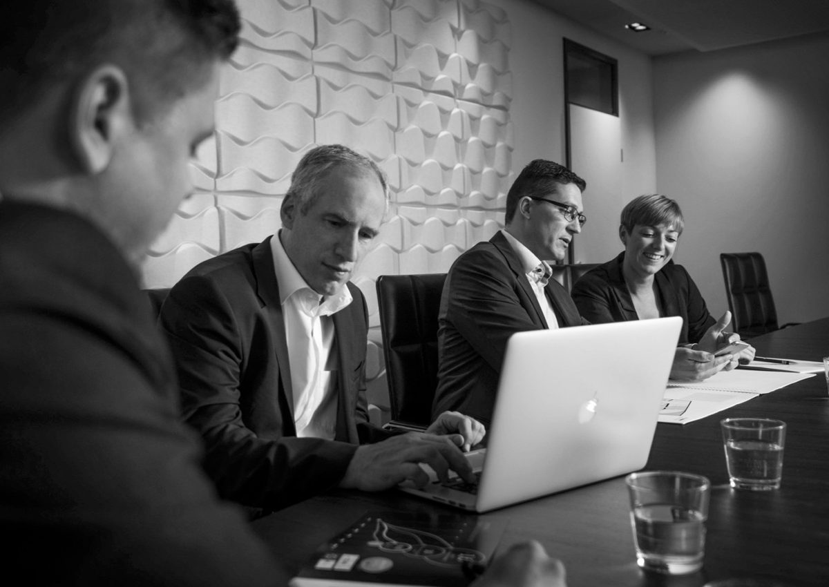 Schwarzweisse Aufnahme einer Besprechung mit vier Personen am Konferenztisch mit Laptop — Das Studiozwei, Werbefotograf München