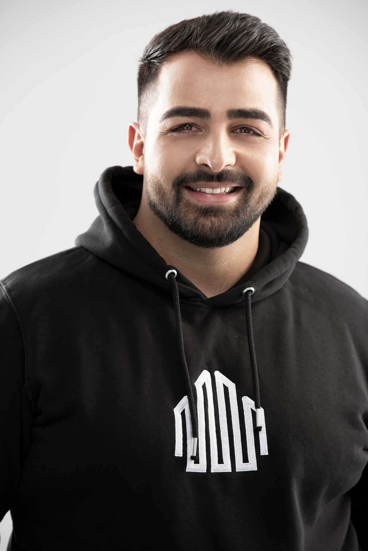 Lachender Mitarbeiter im schwarzen Hoodie mit Firmenlogo — Das Studiozwei, Werbefotograf München