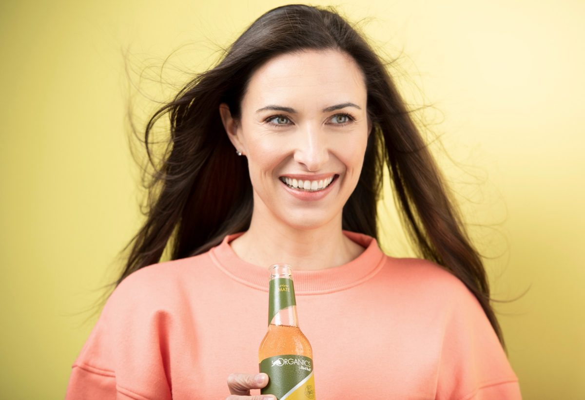 Portraet einer laechelnden Frau mit Getraenkeflasche vor gelbem Hintergrund — Das Studiozwei, Werbefotograf München