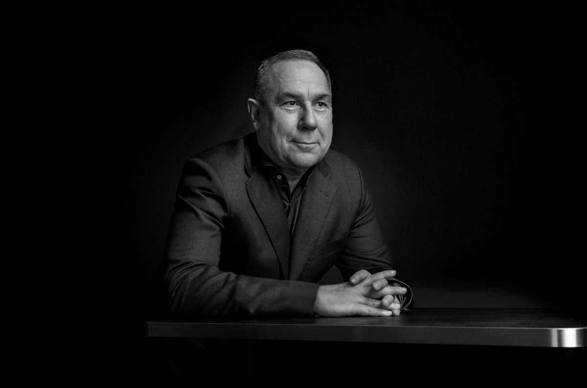 Schwarzweisses Low-Key-Businessportrait eines Mannes im Sakko an einem Tisch — Das Studiozwei, Werbefotograf München
