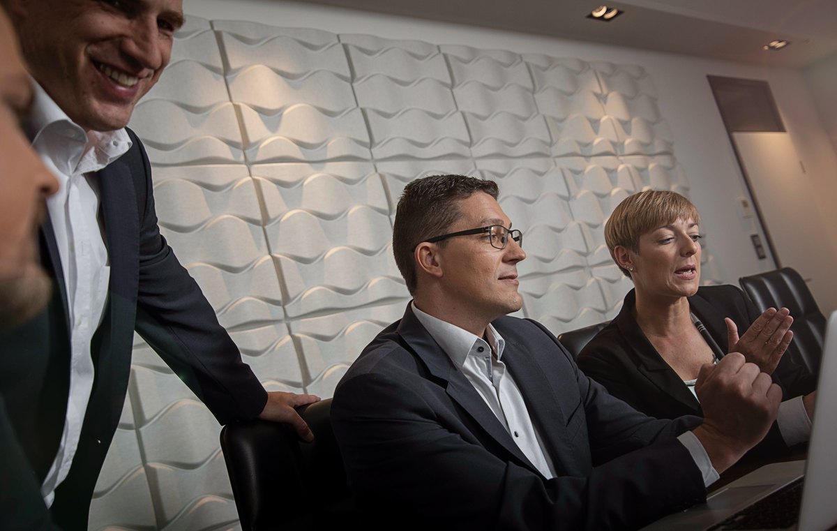 Lachendes Team am Konferenztisch vor weisser Strukturwand — Das Studiozwei, Werbefotograf München