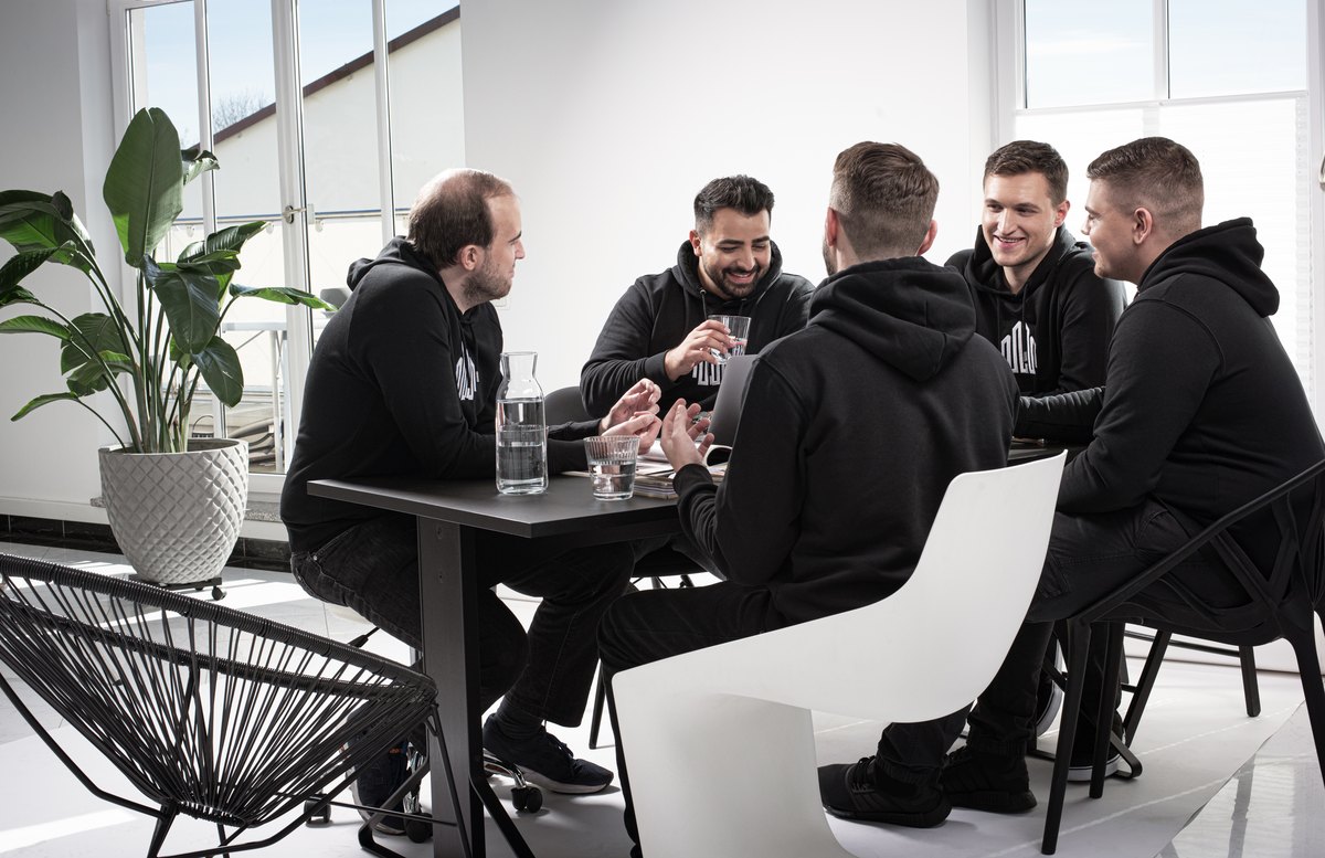 Team am Besprechungstisch in hellem Buero mit Pflanzen — Das Studiozwei, Werbefotograf München