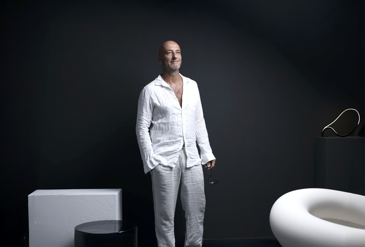 Stehender Mann in weissem Leinenhemd mit Brille in der Hand vor dunkler Wand — Das Studiozwei, Werbefotograf München