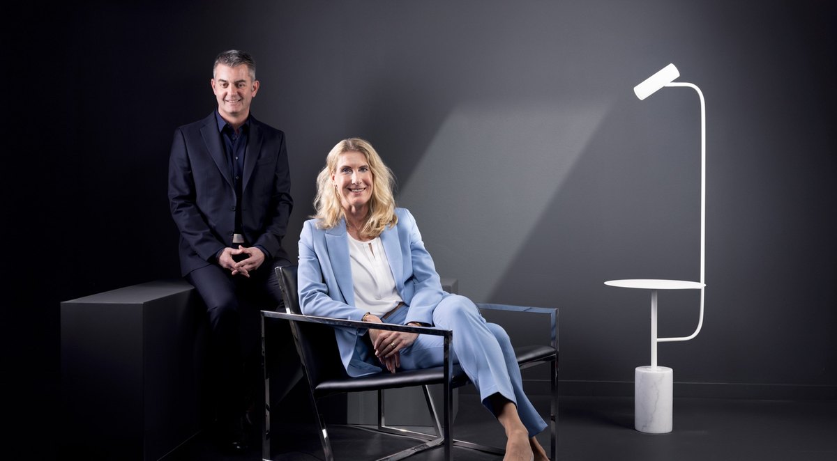 Mann und Frau im Business-Look posieren auf Podest und Lederstuhl vor dunklem Hintergrund — Das Studiozwei, Werbefotograf München