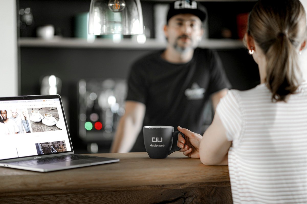 Frau mit Laptop und Kaffeebecher im Gespraech mit Barista an der Theke — Das Studiozwei, Werbefotograf München