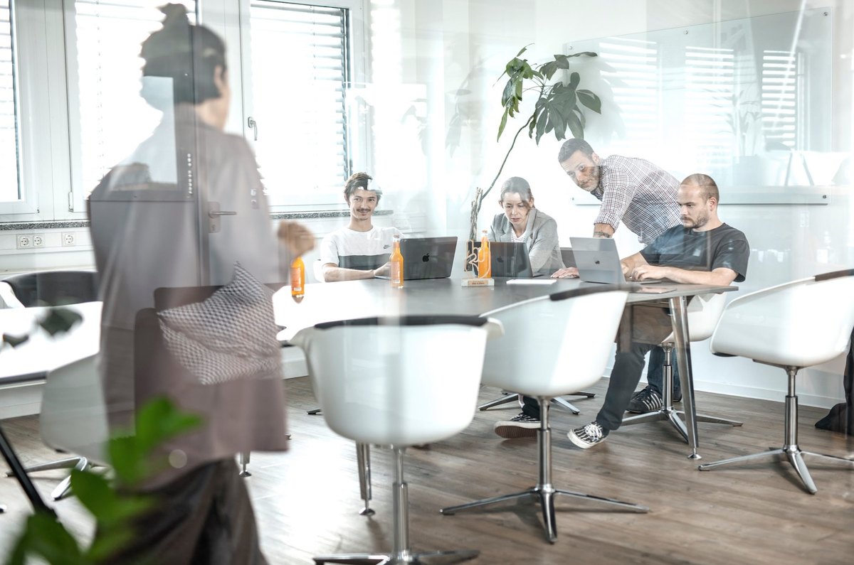 Teambesprechung an rundem Tisch hinter spiegelnder Glaswand im Buero — Das Studiozwei, Werbefotograf München