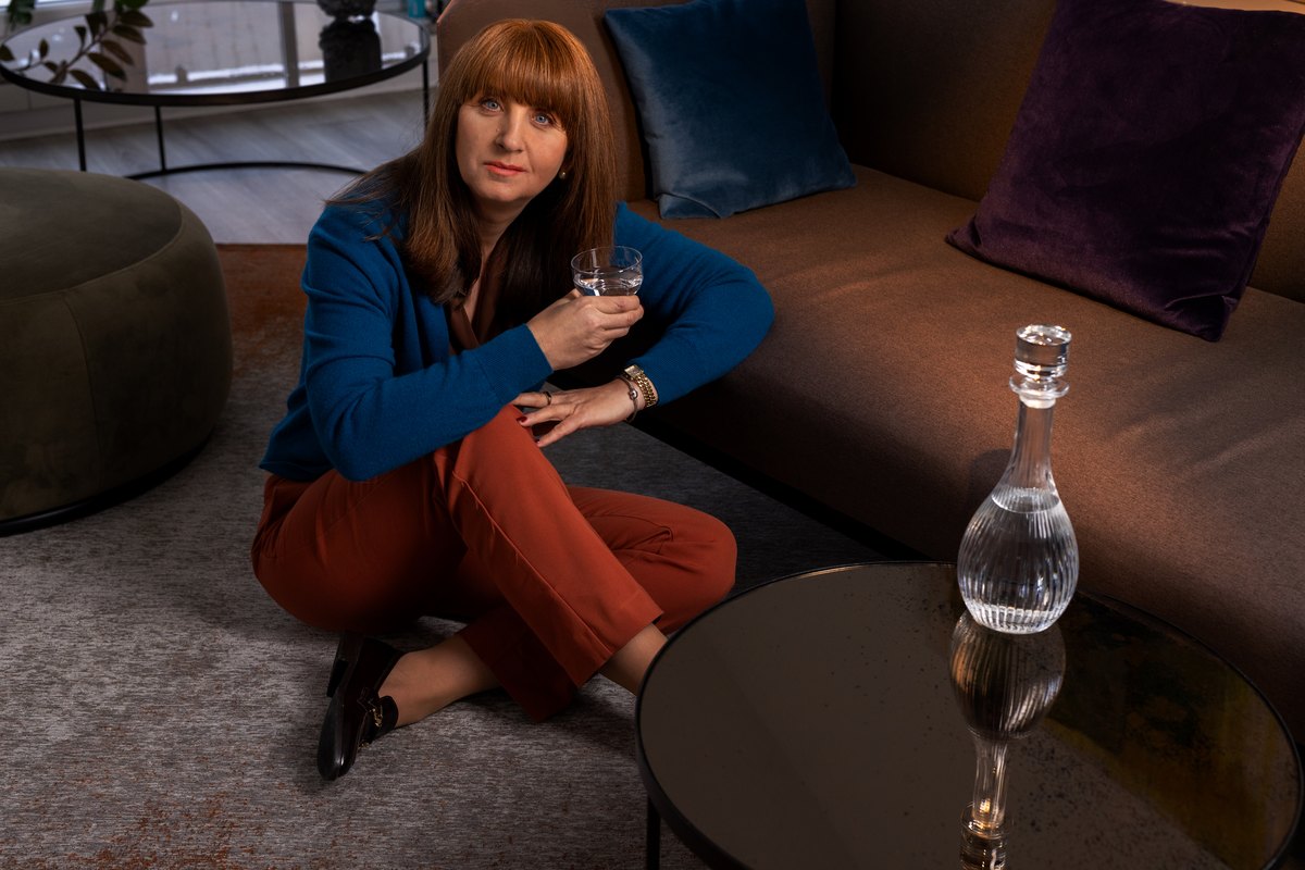Frau in blauem Pullover sitzt am Boden neben Sofa und Glaskaraffe — Das Studiozwei, Werbefotograf München