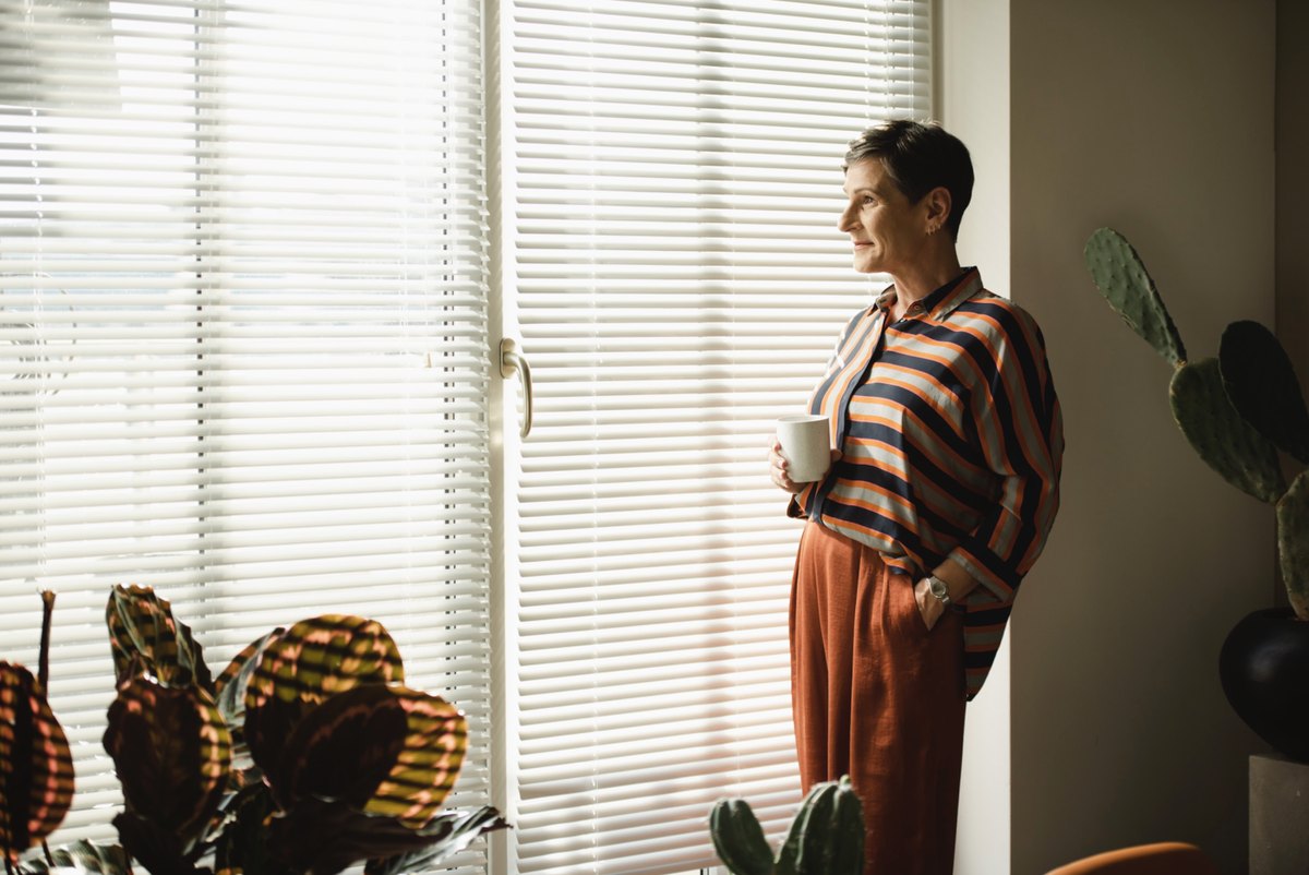 Frau mit Kaffeetasse am Fenster mit Jalousie und Pflanzen — Das Studiozwei, Werbefotograf München