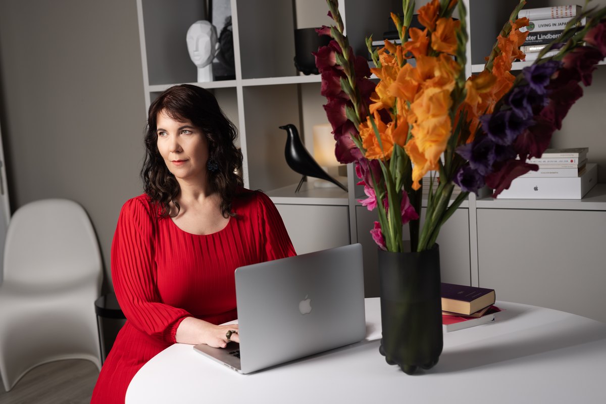 Frau in rotem Oberteil am Laptop neben einem Gladiolenstrauss — Das Studiozwei, Werbefotograf München