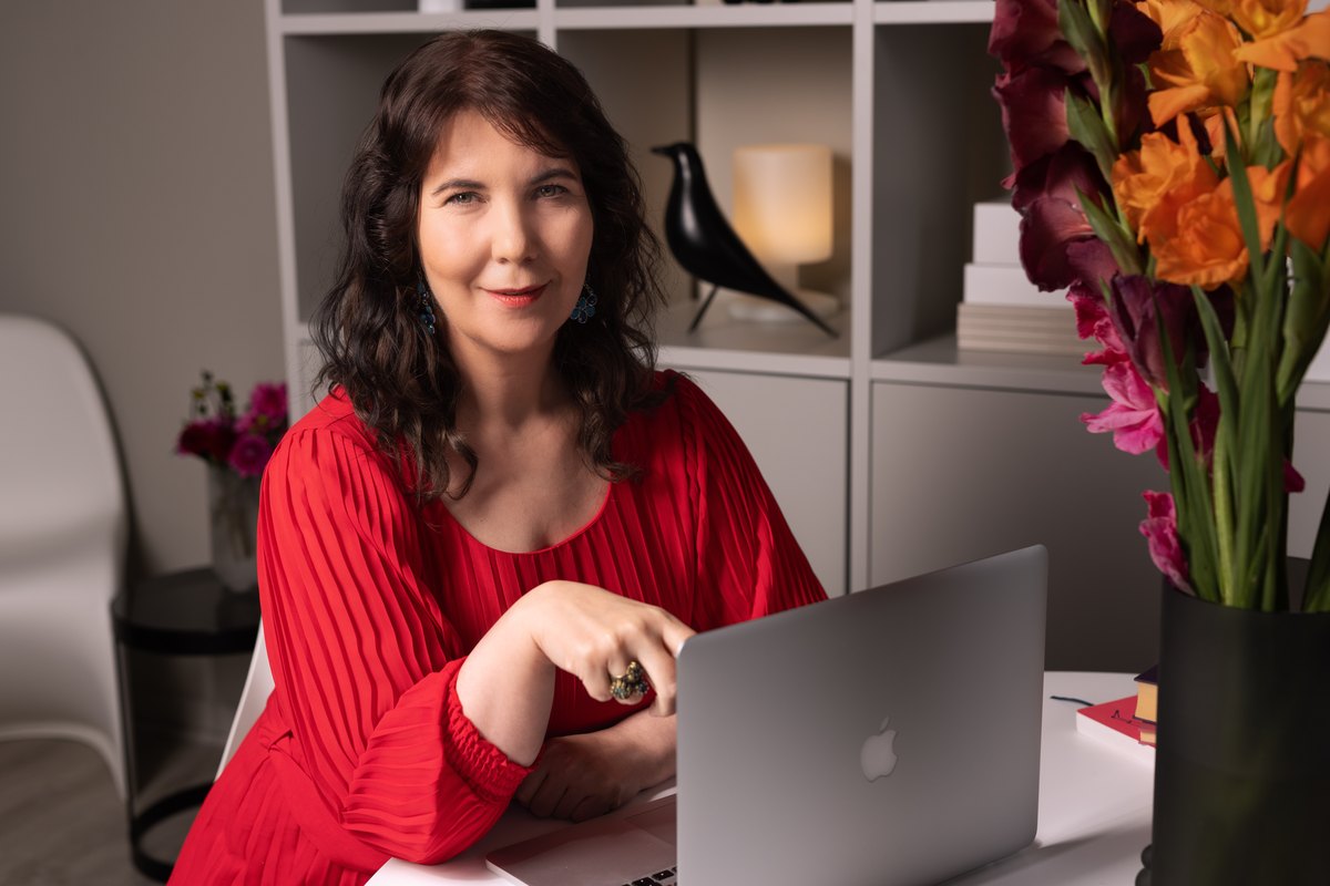 Frau in rotem Oberteil arbeitet am Laptop, Blumen im Vordergrund — Das Studiozwei, Werbefotograf München