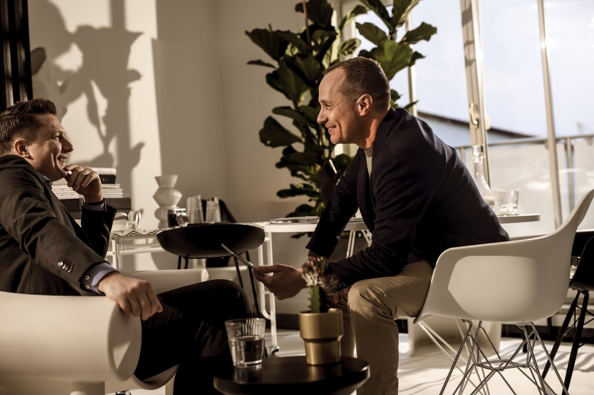 Zwei Maenner im Gespraech in heller Lounge mit Pflanzen — Das Studiozwei, Werbefotograf München