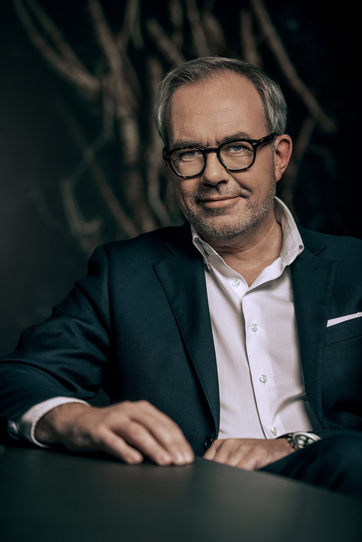 Mann mit Brille im gruenen Sakko stuetzt sich auf einen Tisch — Das Studiozwei, Werbefotograf München