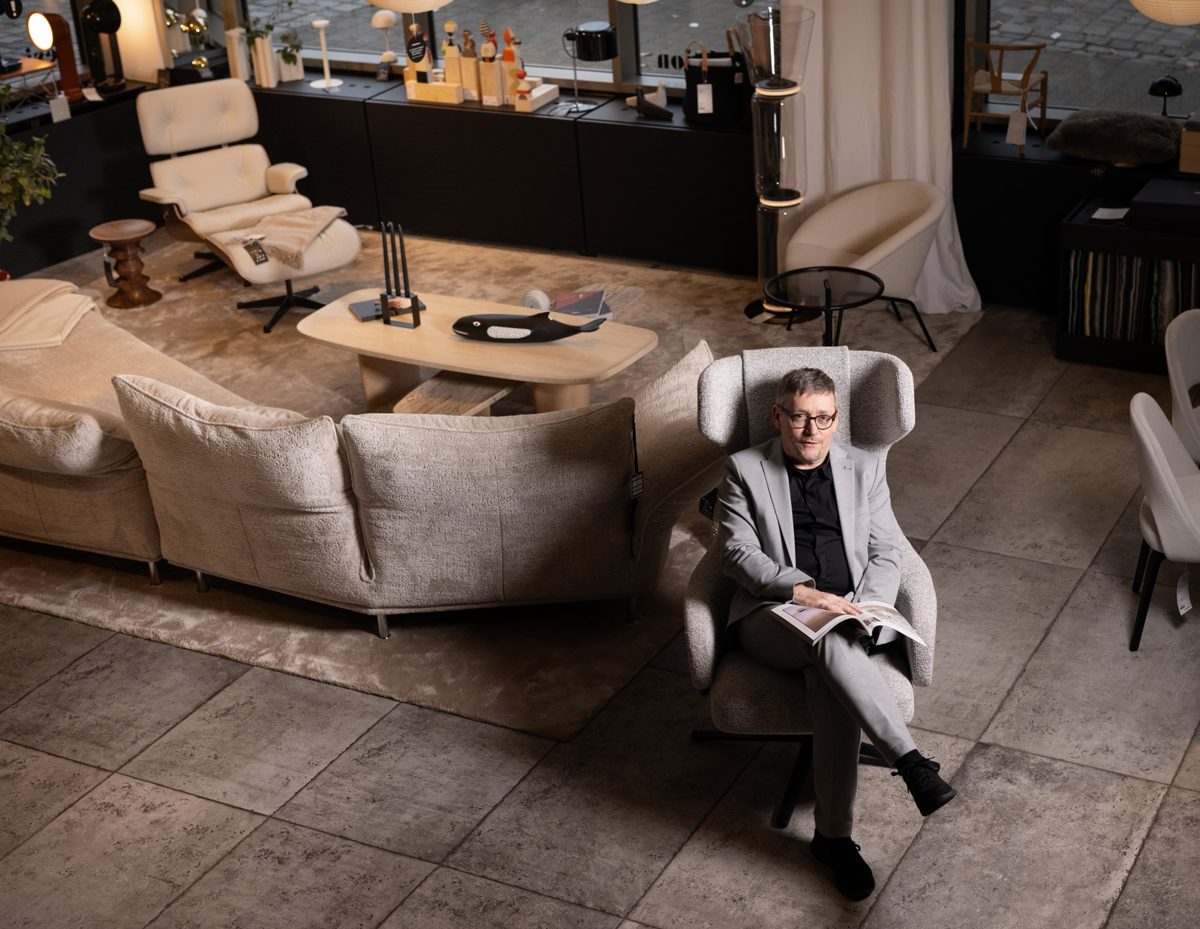 Mann im hellen Anzug sitzt mit Magazin in einem Sessel in einem Moebel-Showroom — Das Studiozwei, Werbefotograf München