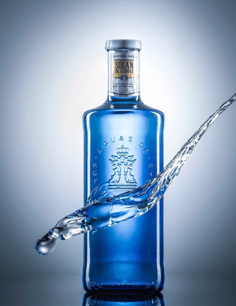 Blaue Glasflasche mit Wasserstrahl vor grau-blauem Studiohintergrund — Das Studiozwei, Werbefotograf München