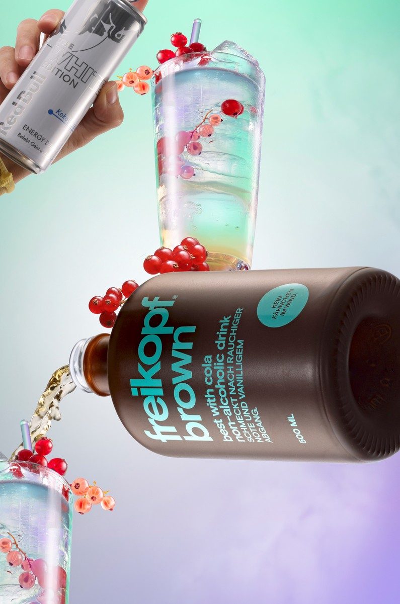 Schwebende braune Getraenkeflasche mit Bechern, Eis und Johannisbeeren vor mint-fliederfarbenem Verlauf — Das Studiozwei, Werbefotograf München