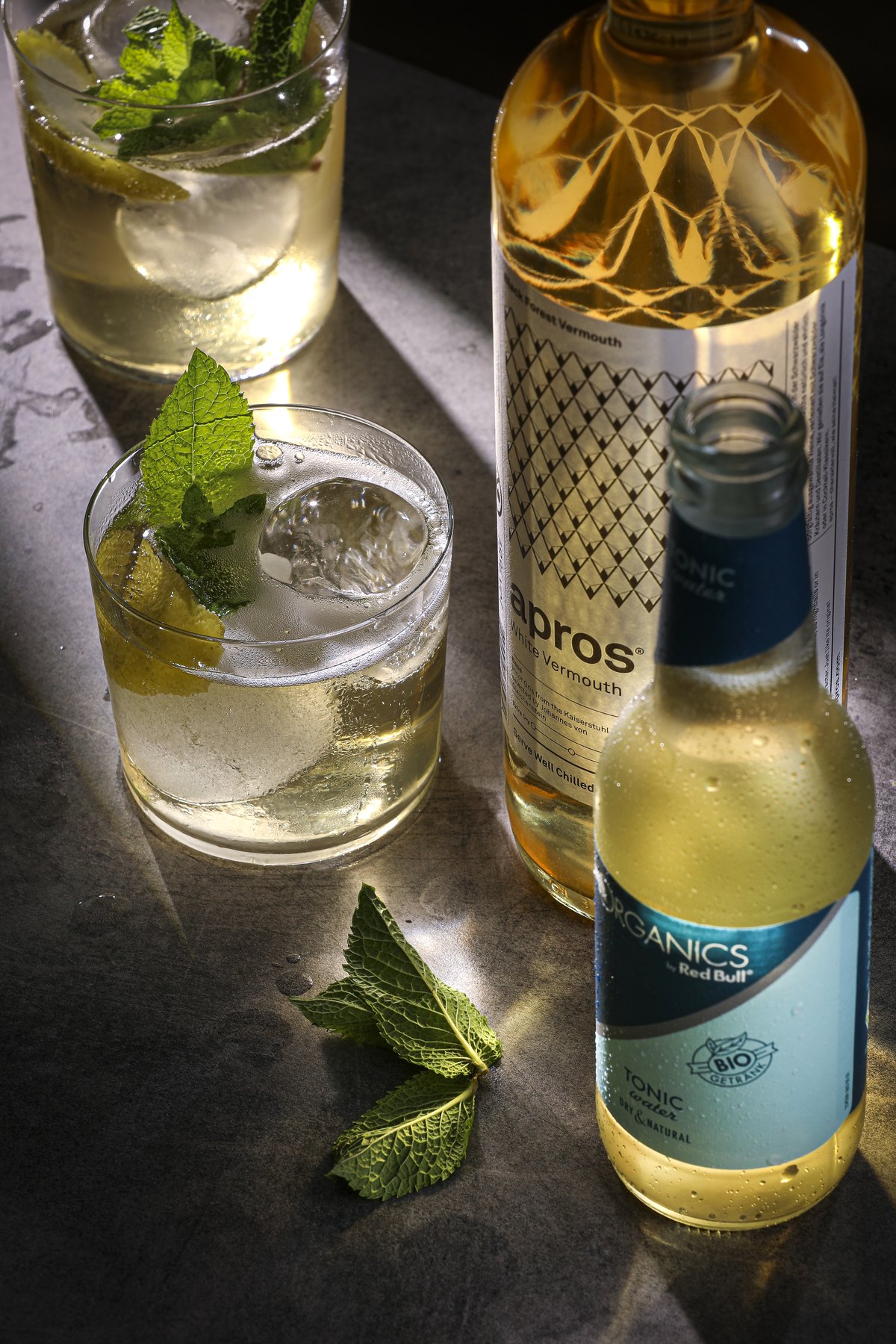 Gin-Flasche mit zwei Glaesern, Minze und Limette im Streiflicht — Das Studiozwei, Werbefotograf München