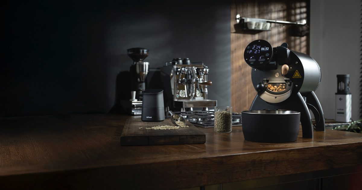 Schwarzer Kaffeeroester mit leuchtendem Display auf einer Holztheke vor dunklem Hintergrund — Das Studiozwei, Werbefotograf München