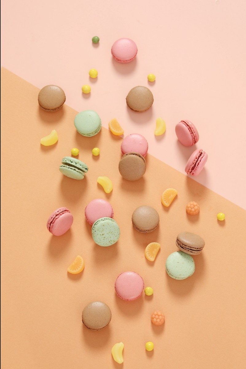 Flatlay mit pastellfarbenen Macarons und Bonbons auf rosa und apricotfarbenem Hintergrund — Das Studiozwei, Werbefotograf München